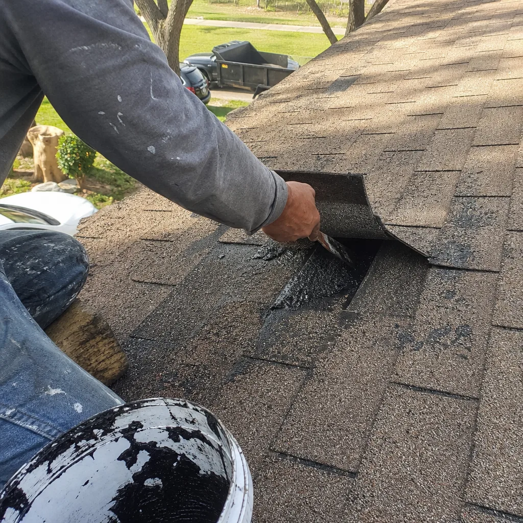 A roofing professional applying sealant to repair shingles on a residential roof.